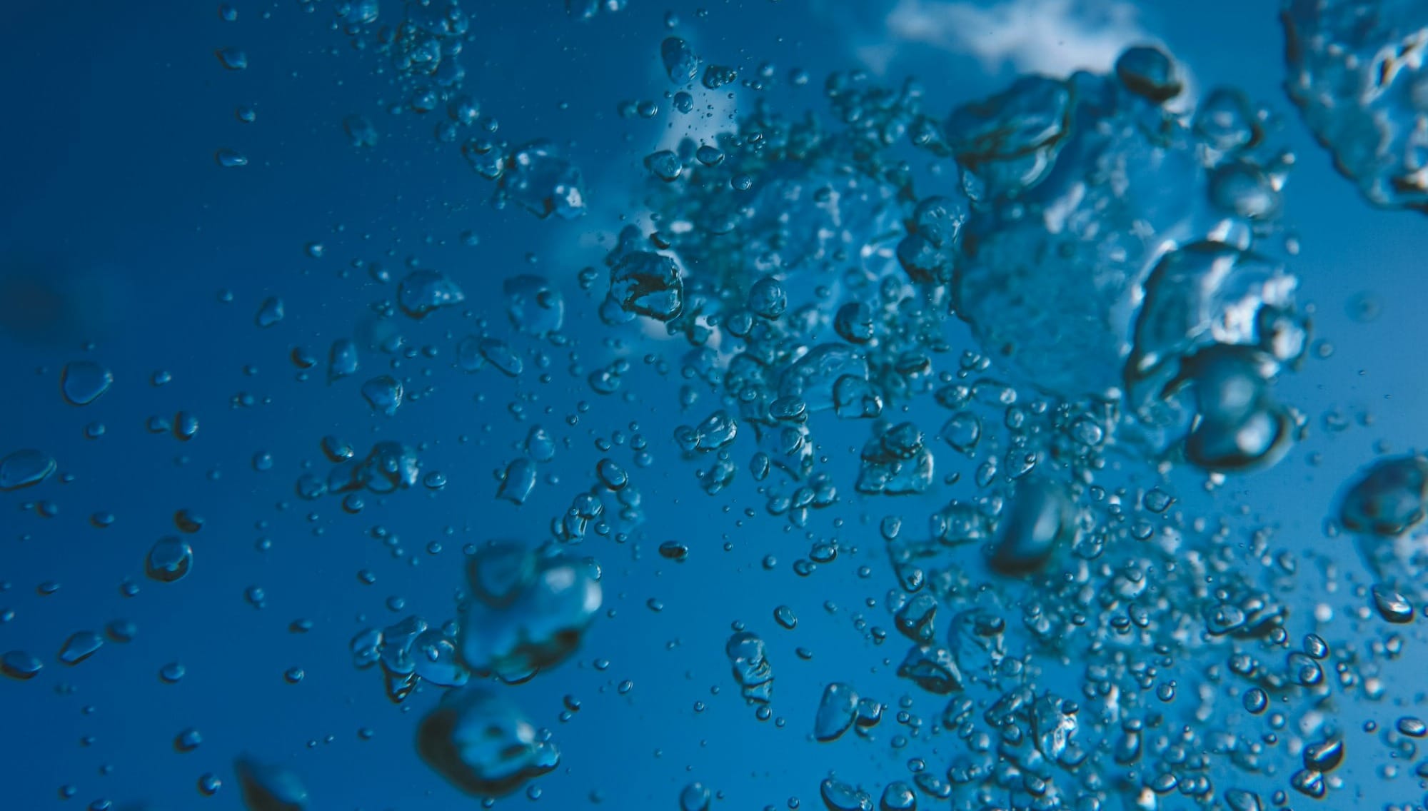 Bubbles rising in clear blue water towards sky