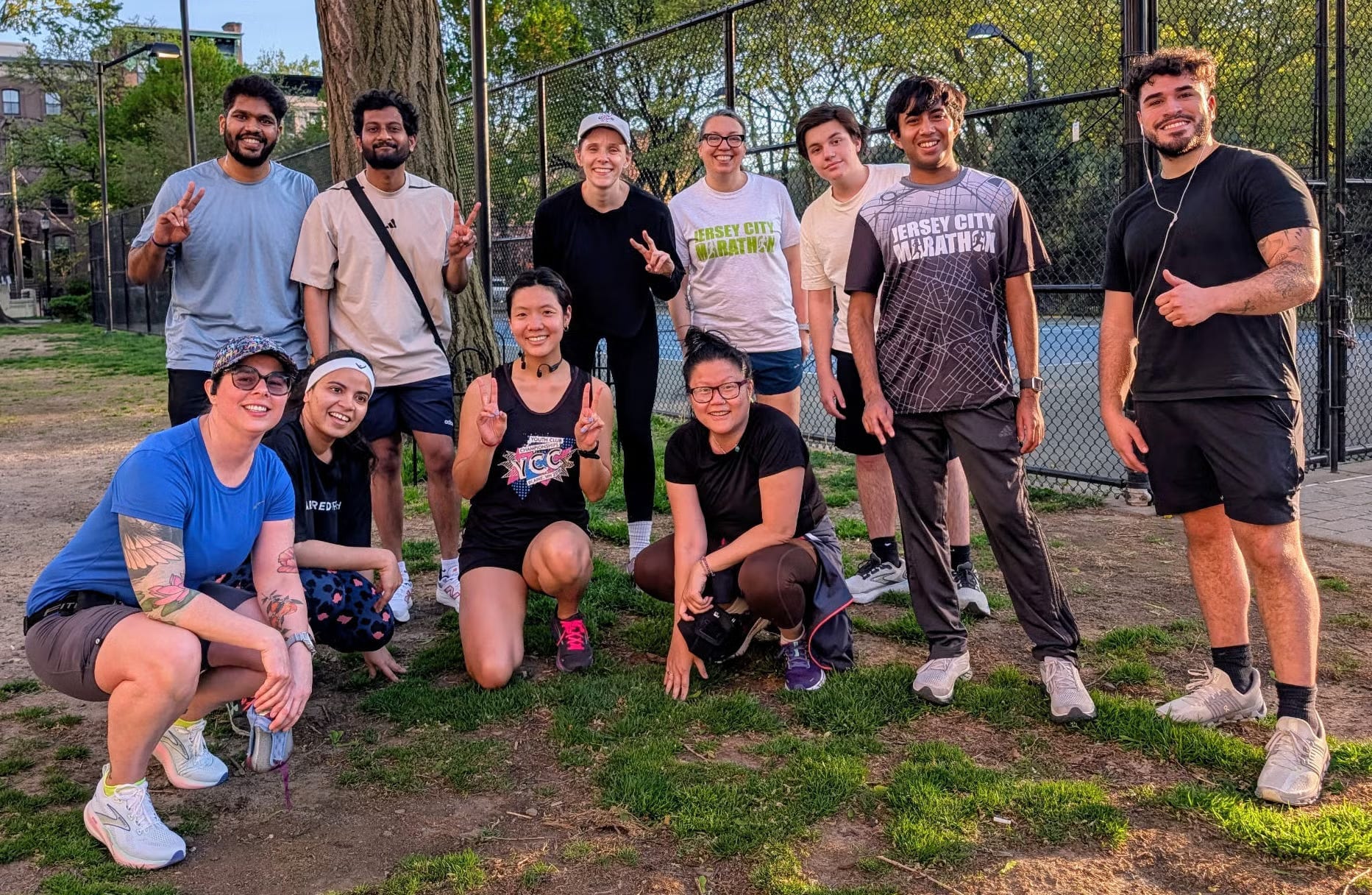 A group of runners stands and kneels around a tree on a sunny day for a photo.