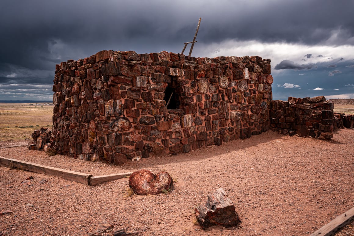 Agate House, a reconstructed ancestral Puebloan structure made of colorful petrified wood, surrounded by desert terrain in Petrified Forest National Park, Arizona.