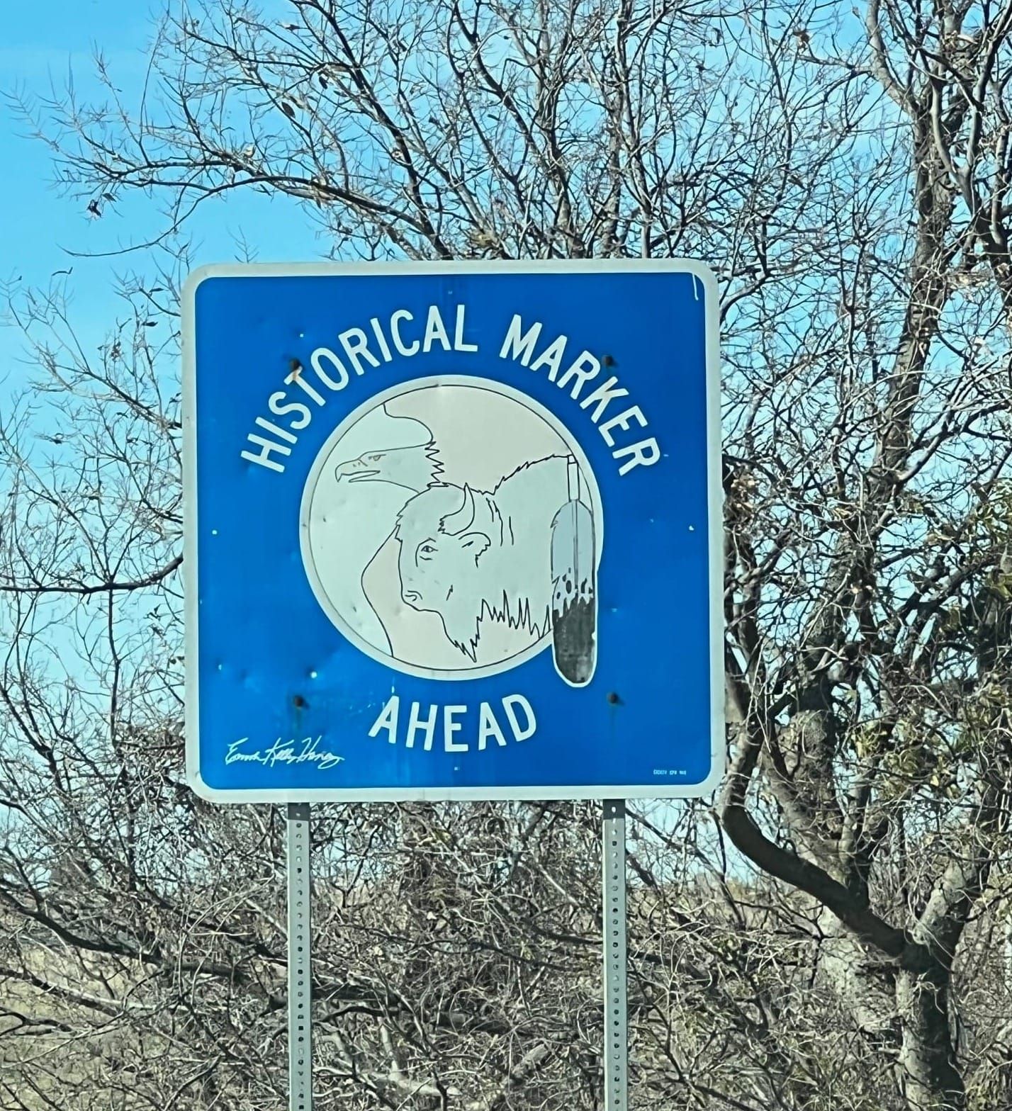 Historial Marker Ahead sign outside El Reno, Oklahoma. It is blue, with images of an eagle, buffalo, and ceremonial feather.