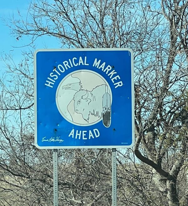 Historial Marker Ahead sign outside El Reno, Oklahoma. It is blue, with images of an eagle, buffalo, and ceremonial feather.