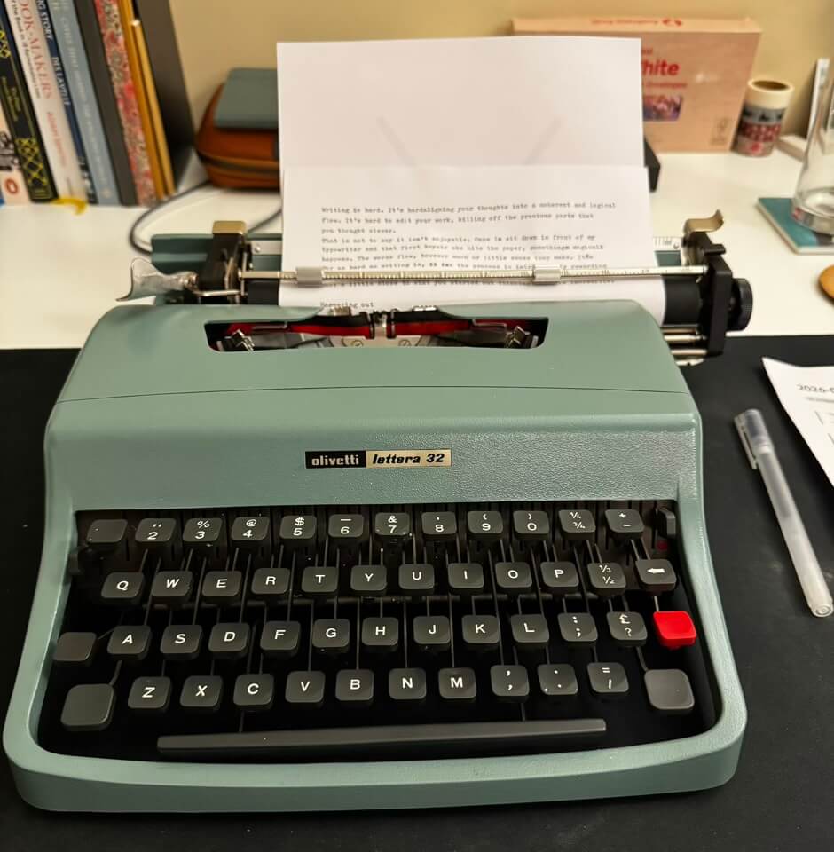 A green Olivetti Lettera 32 typewriter, with two paragraphs typed on the page loaded into it