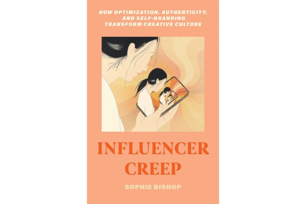 Cover of Influencer Creep by Sophie Bishop. A woman looking at herself on her phone, in a salmon pink cover