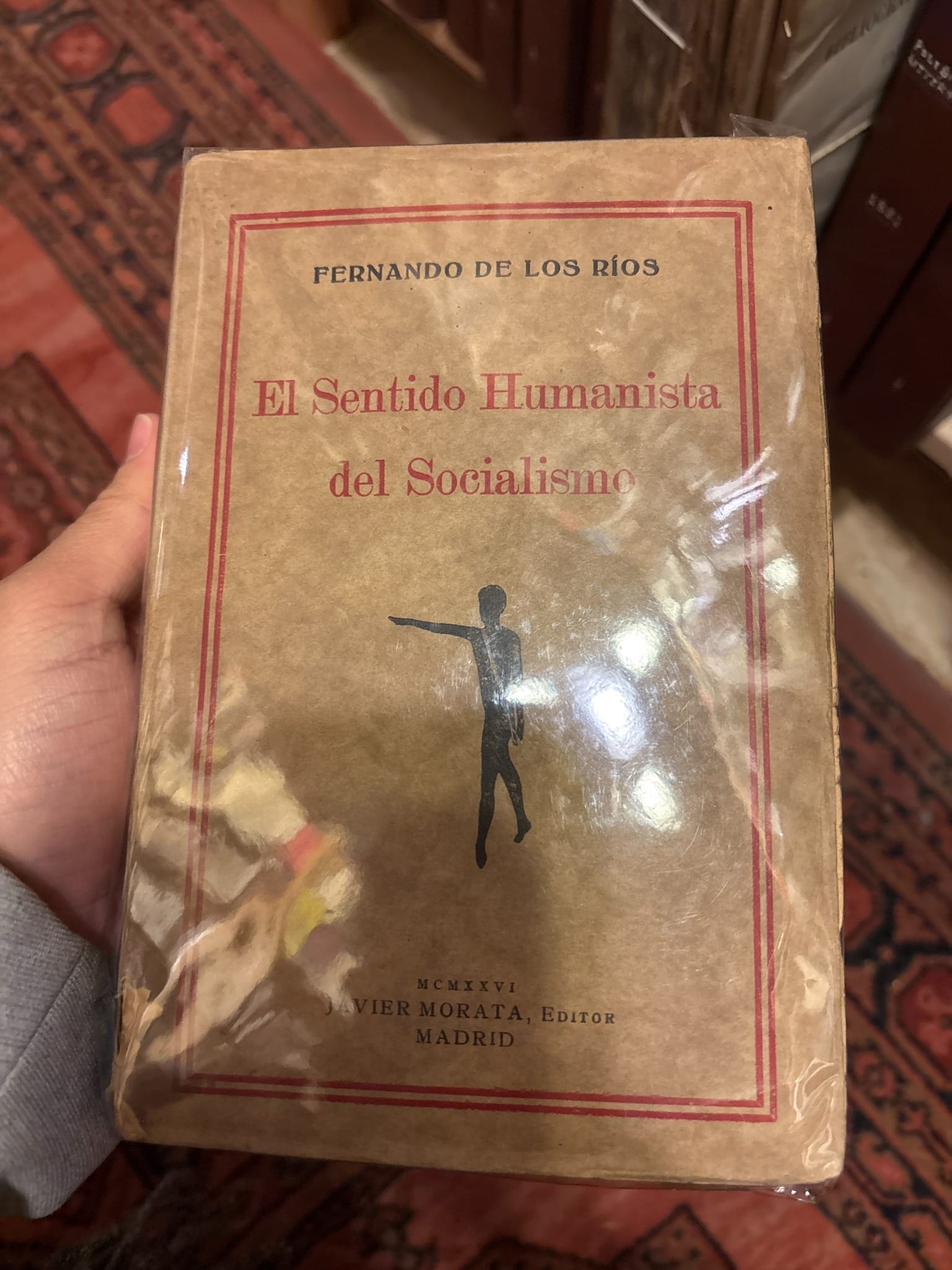 A hand holds El Sentido Humanista del Socialismo by Fernando de los Ríos, with a worn cream and red cover.