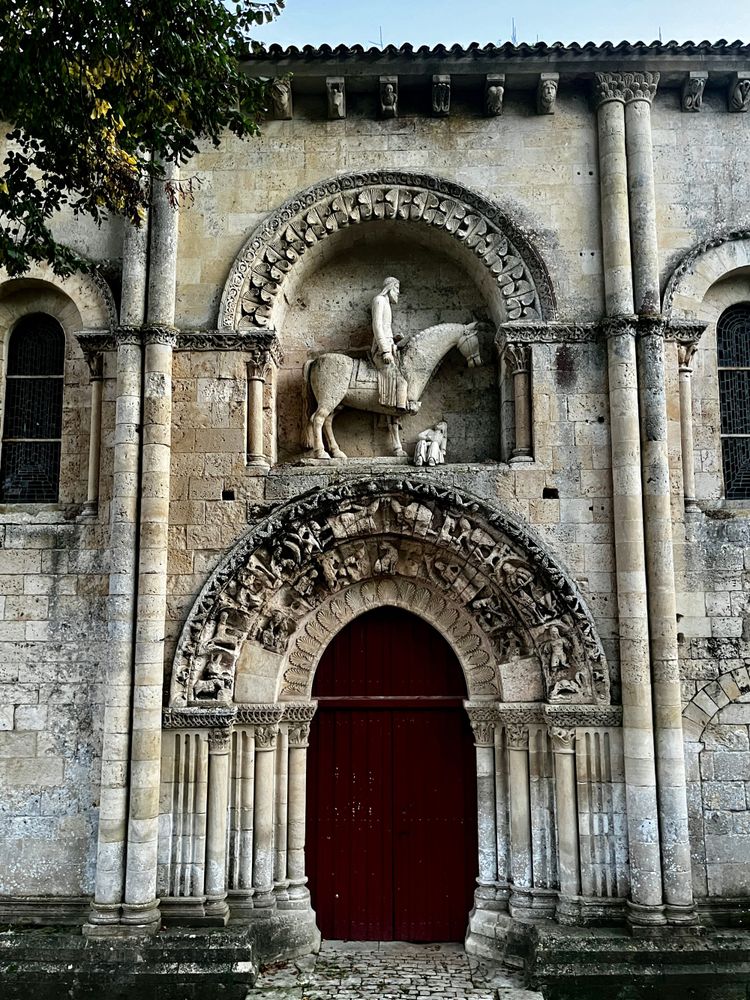 Roman catholic church entryway with sculptures over the door of a horse about to step on what looks like a poor helpless wom