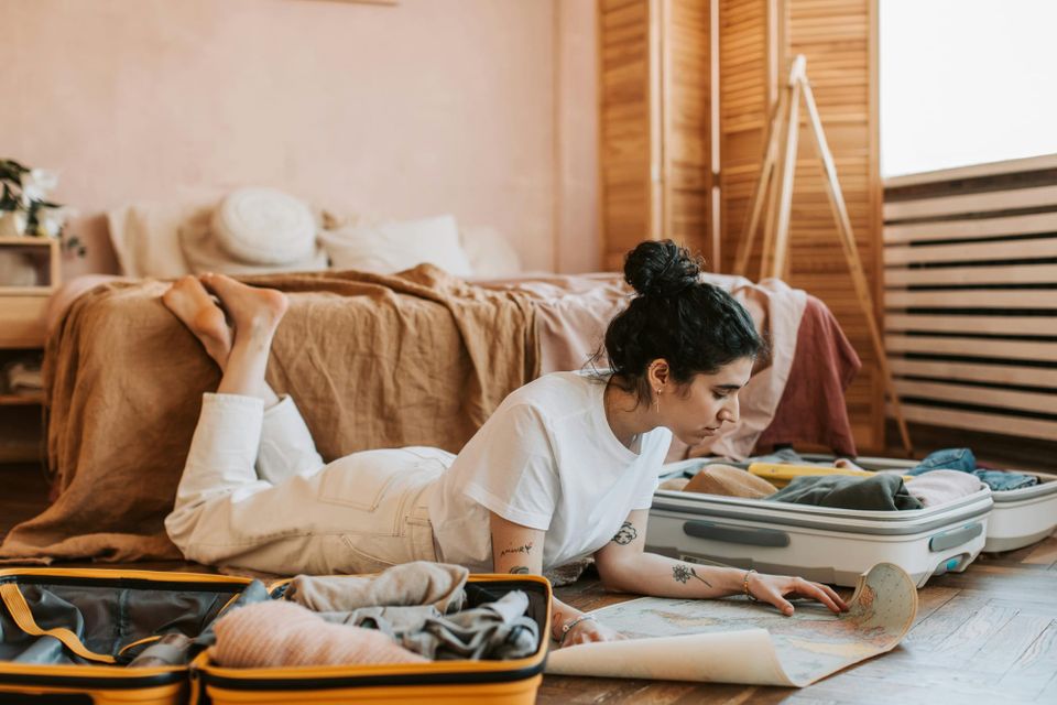 Young woman packing a suitcase and reading maps in her bedroom, preparing for an exciting travel adventure.