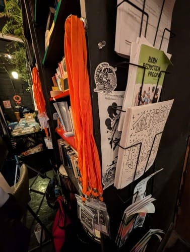 Orange security lanyards and activist zines on a rack beside a bookshelf.