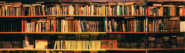 Photo of a long bookshelf with book stacked in many ways. 