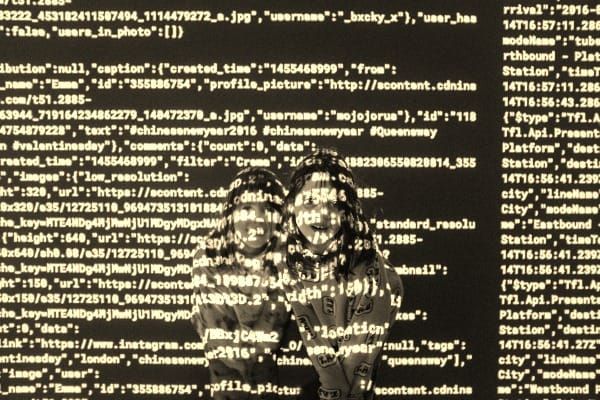Lines of computer code written across the images of two happy girls, the code moves over them as if in three dimensions.