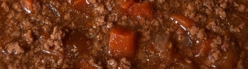 A close-up of some oily, brown mince with chunks of what once may have been vegitable in it.