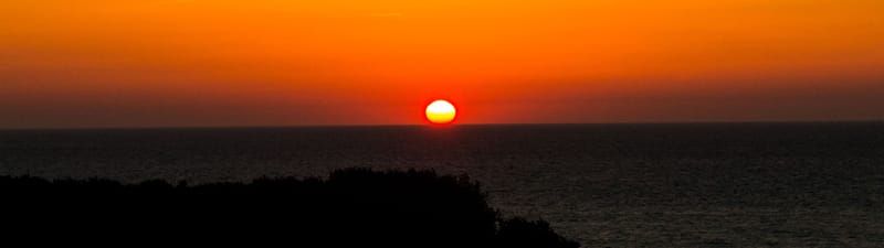 An image of a sun rising over the horizon. It is orange and yellow. Image from Creative Commons Wikimedia.