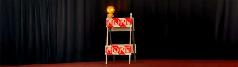 A US-style construction barrier with a yellow warning light on top, with the word HOPE in capital letters written across it.