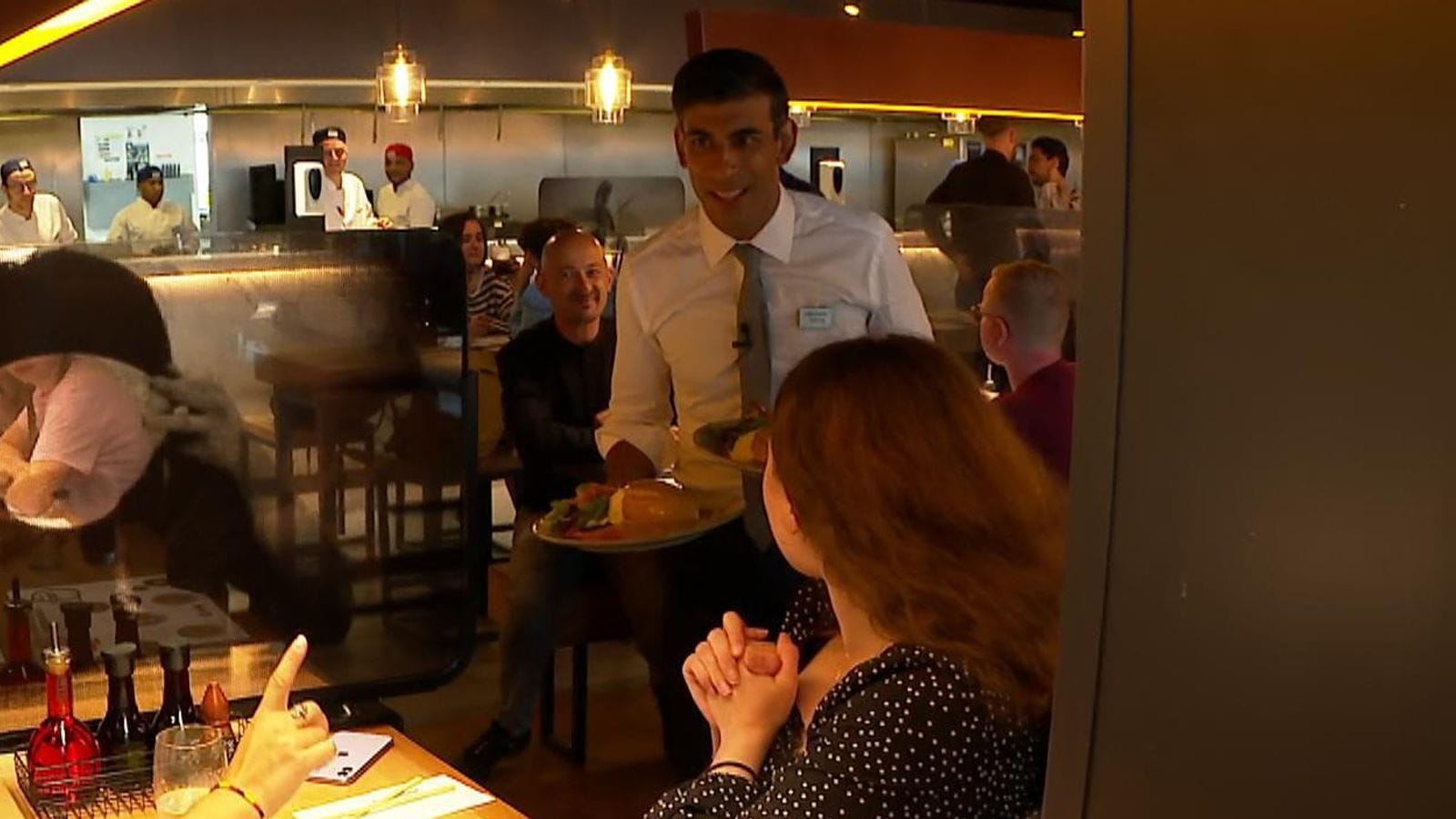 A grinning Rishi Sunak offering plates of food to people in restaurants as a virus rages.