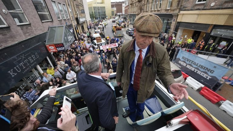 Nigel Farage on the top of an open top bus with a small crowd in the street
