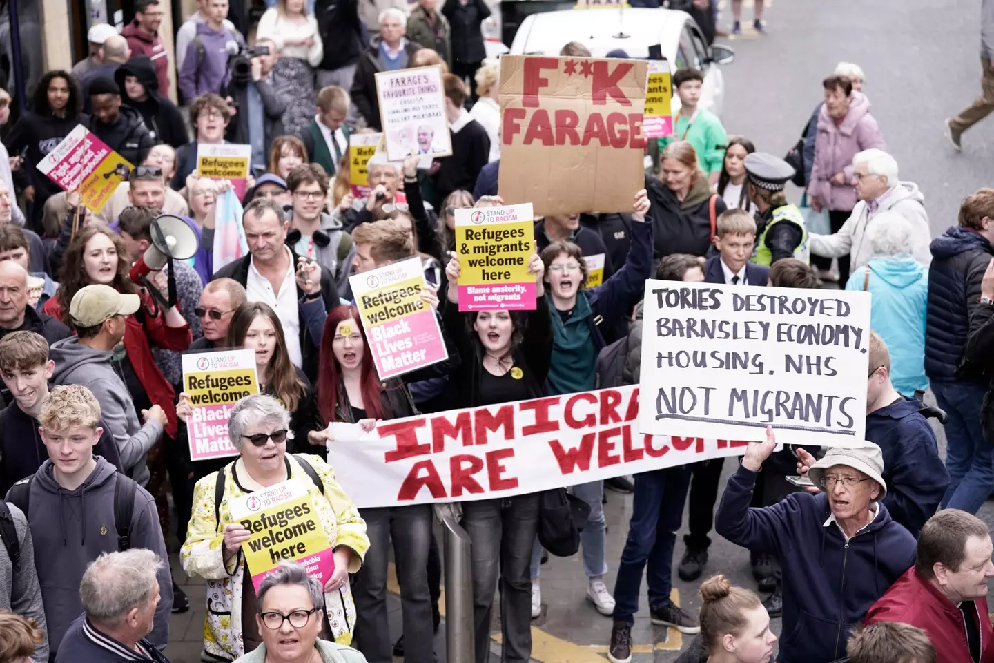 The same small crowd, bearing signs such as "refugees welcome," "fuck Farage," "Tories destroyed Barnsley economy, housing, NHS, not migrants," and "immigrants are welcome"