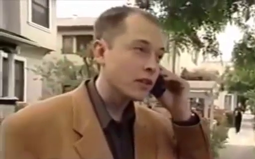 A balding young man in an oversized jacket awkwardly answering a mobile phone in a street