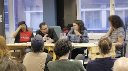 Four people at a table with microphones before a seated audience.
