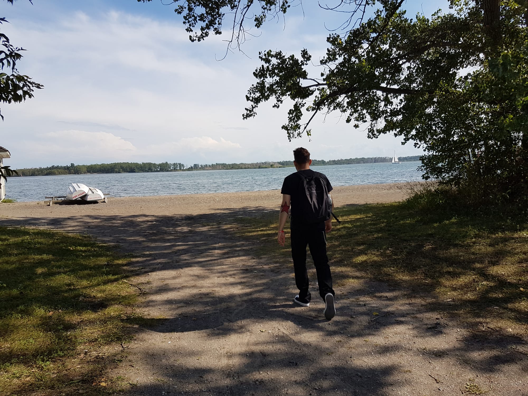Me, a white person with a red star tattoo on the left elbow, wearing a backpack, heading towards a beach.