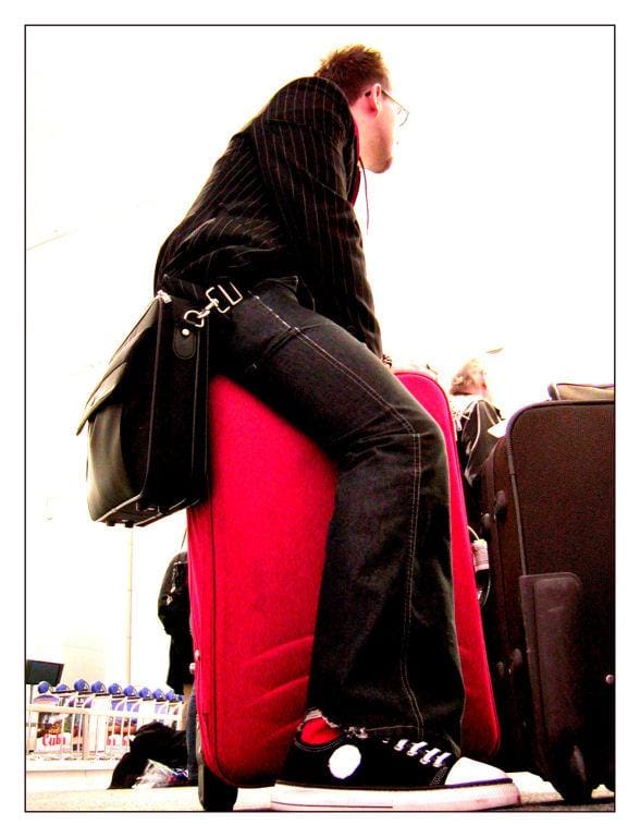 Me, a white person with dark hair and goatee, sat on a suitcase in an airport.