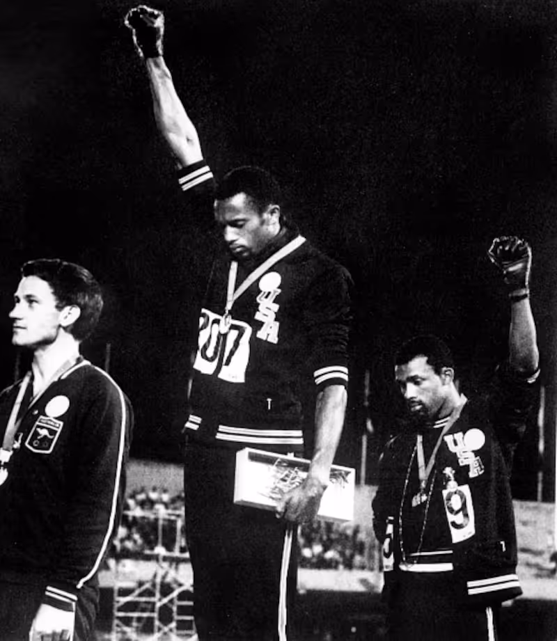 Tommie Smith and John Carlos standing on the 1968 Olympic medalists’ podium, raising their fists.