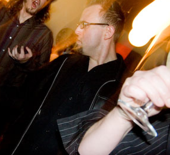 Me, a white person with glasses, dark hair, and goatee, pulling a face while dancing amongst other people dancing and drinking.