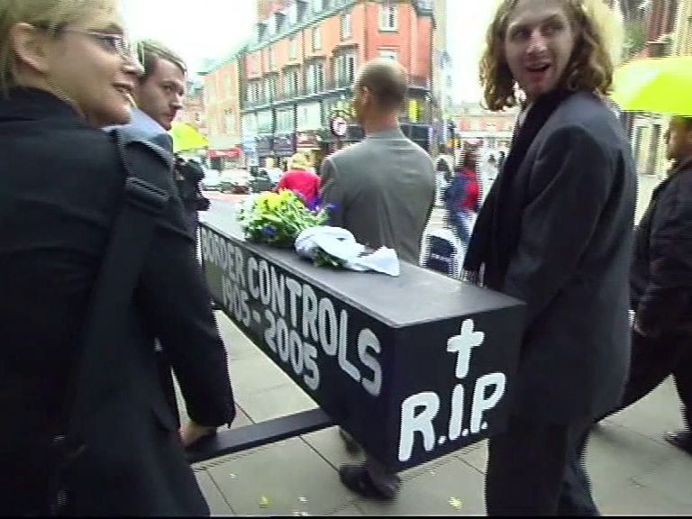 People in suits carrying a coffin bearing writing "border controls 1905-2005 RIP"