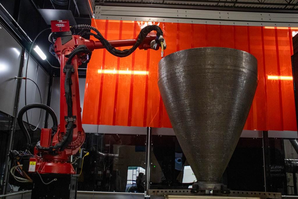 A robotic wire arc additive manufacturing system uses a welding torch to deposit metal wire layer by layer, forming a large near-net-shape metal structure.