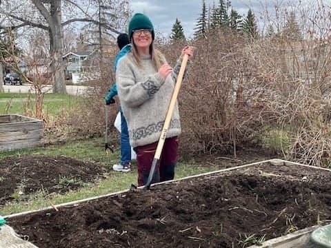 Woman holding shovel in front of wooden raised garden bed