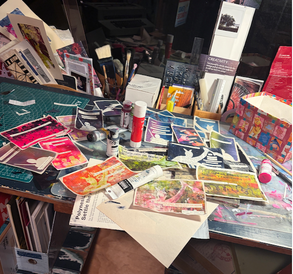 My desk covered in paint, gelli-prints, and collage - and a mountain of postcards with quotes on them!