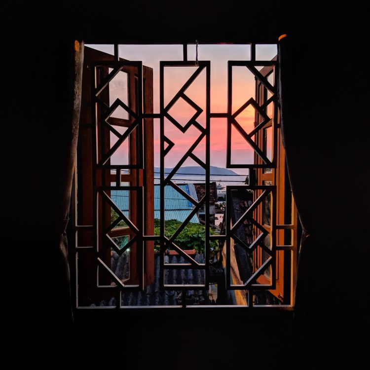 Looking out a decorative window to a sunset over the distant ocean