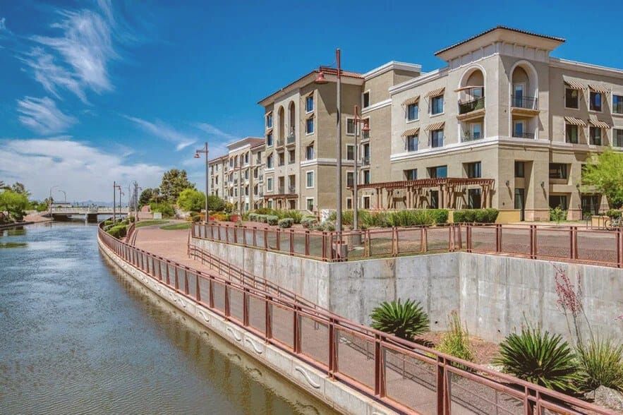 Wide aerial view of a glass high-rise tower along a desert urban canal at midday, blue sky, no people