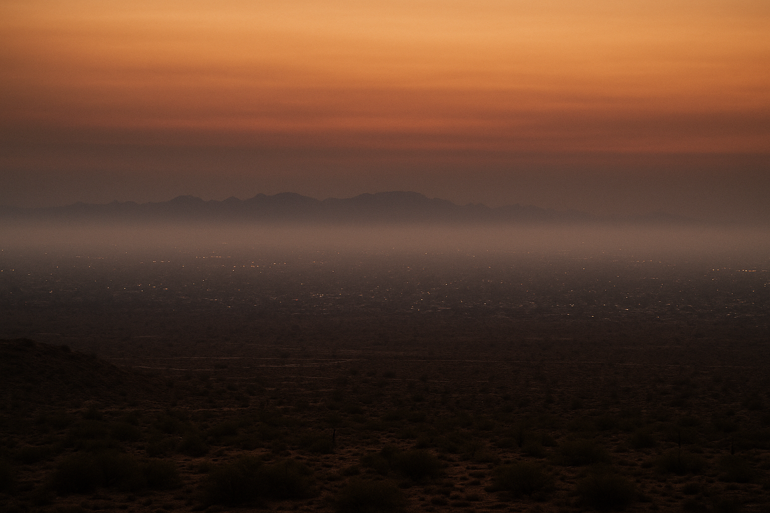 Wide aerial view of a hazy desert basin at pre-dawn, orange-tinged sky, no people, no text