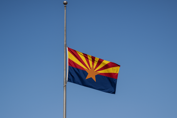 Arizona state flag at half-staff on a flagpole against a clear blue sky, no people