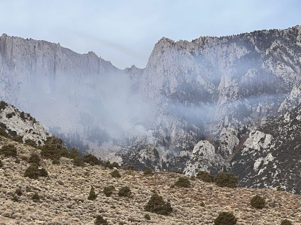 view of a desert brush landscape with faint smoke rising from a dry hillside near a reservoir, late afternoon light, no peopl