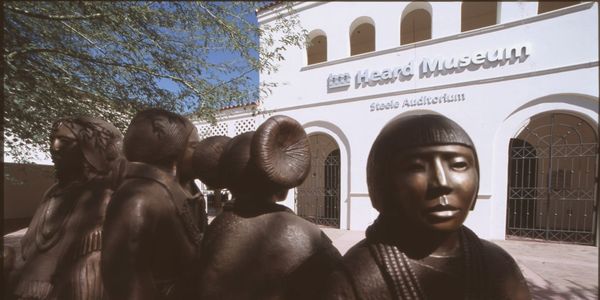 of a sunlit museum courtyard with desert plantings, a stone sculpture on a low plinth, and terracotta-toned walls in the back