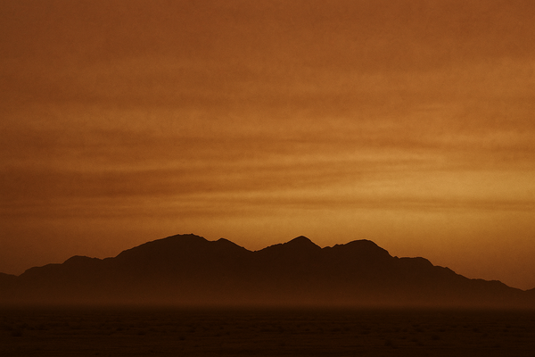 of a hazy desert sky at dusk over a low desert ridgeline, orange and brown tones, no people
