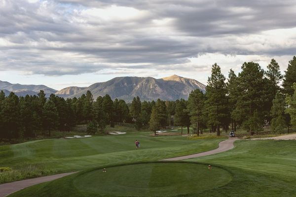 Wide aerial view of a pine-forested mountain golf course at golden hour, no people, no text, soft clouds over distant peaks