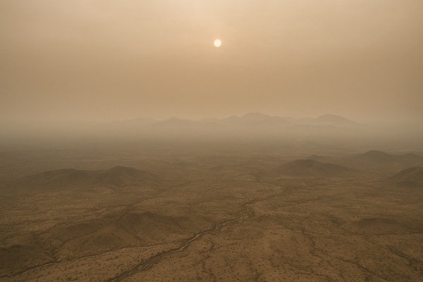 Wide aerial view of a hazy brown sky over a desert valley at midday, sun diffused through smog, no people or identifiable str