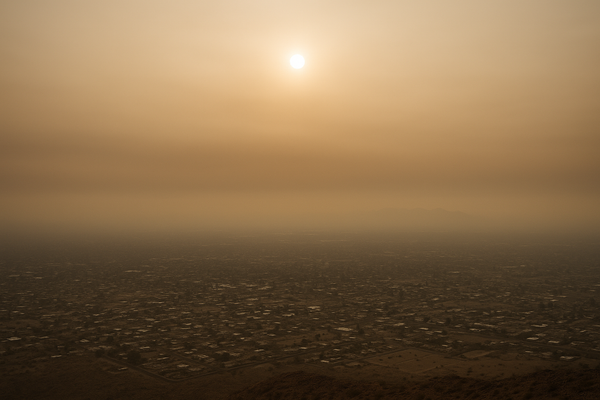 of a hazy desert sky over a flat urban valley at midday, sun diffused through brownish-orange smog, no people