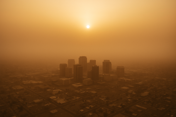 Wide aerial view of a hazy desert city skyline at dusk, orange-brown particulate haze visible in the air, no people, no text