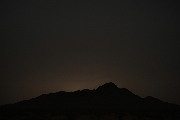 Wide desert sky at night over a dark mountain ridgeline, faint haze visible in the air, no people