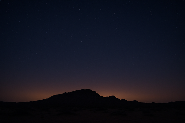 Wide desert sky at night over a dark ridgeline, faint orange haze visible near the horizon, no people