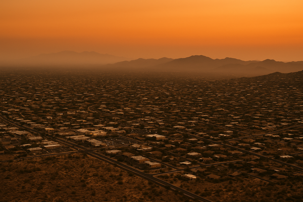 Wide aerial view of a desert town at dusk, hazy orange sky, low mountains in the background, no people