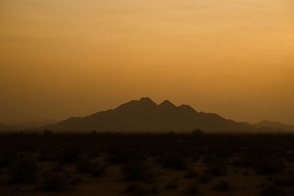 Wide desert sky over a dry Sonoran landscape at dusk, hazy orange-brown horizon, McDowell Mountains silhouette in the distanc