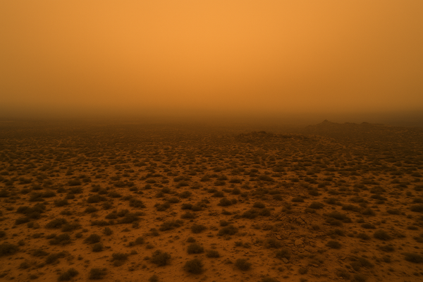 Wide aerial view of a desert landscape at dusk, hazy orange sky over low scrub and rocky terrain, no people, no text