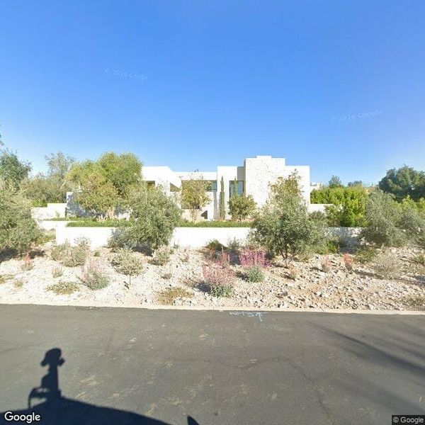 view of a modern desert estate on a flat one-acre lot, pool visible, surrounded by desert landscaping and a low perimeter wal
