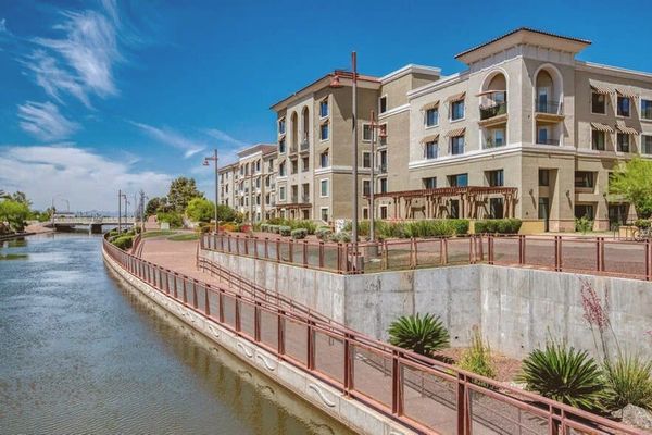 Wide aerial view of a glass high-rise tower along a desert urban canal at midday, blue sky, no people