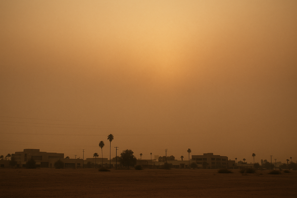of a hazy desert sky at dusk over a flat urban landscape, orange and brown tones, no people, no text