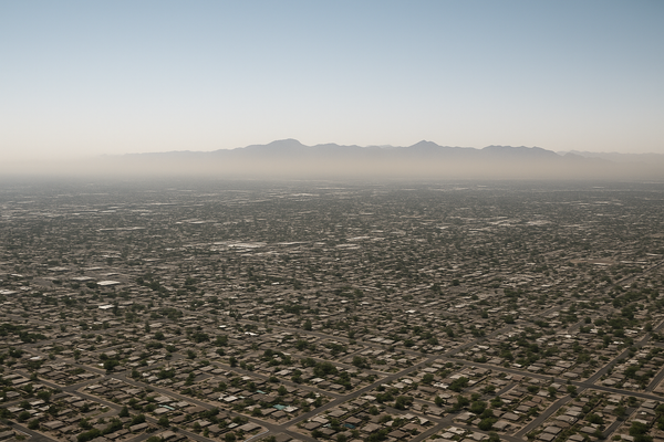 Wide aerial view of a hazy Phoenix valley at midday, brown particulate haze hanging over a flat desert cityscape, no people