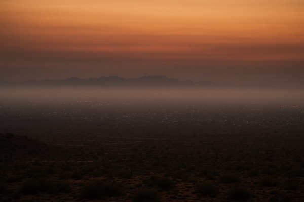 Wide aerial view of a hazy desert basin at pre-dawn, orange-tinged sky, no people, no text